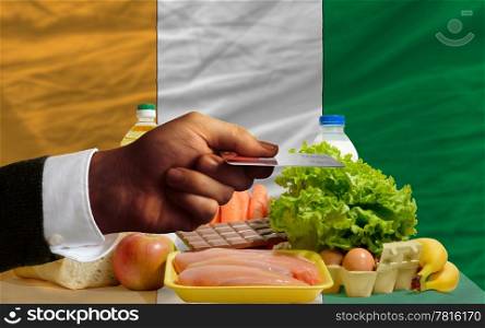 man stretching out credit card to buy food in front of complete wavy national flag of ivory coast