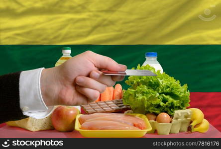 man stretching out credit card to buy food in front of complete wavy national flag of lithuania