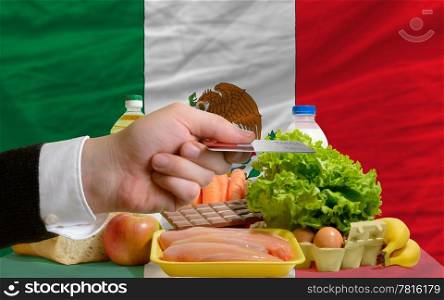 man stretching out credit card to buy food in front of complete wavy national flag of mexico