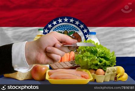 man stretching out credit card to buy food in front of complete wavy american state flag of missouri