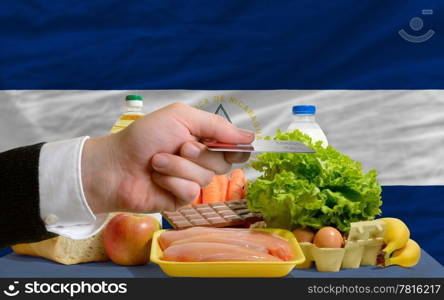 man stretching out credit card to buy food in front of complete wavy national flag of nicaragua