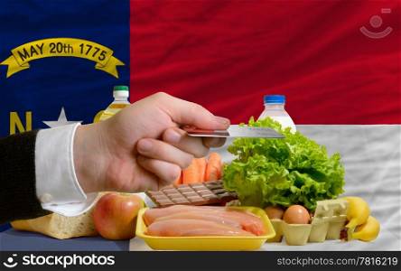 man stretching out credit card to buy food in front of complete wavy american state flag of north carolina