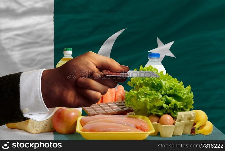 man stretching out credit card to buy food in front of complete wavy national flag of pakistan