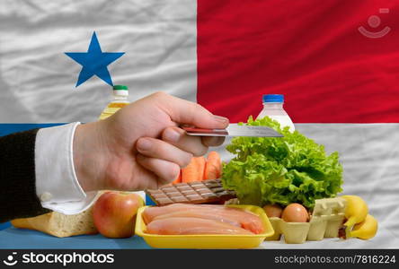 man stretching out credit card to buy food in front of complete wavy national flag of panama