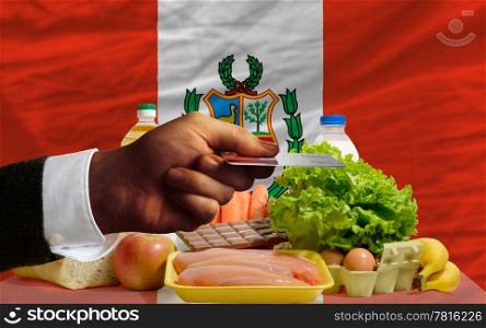 man stretching out credit card to buy food in front of complete wavy national flag of peru