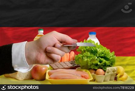 man stretching out credit card to buy food in front of complete wavy national flag of germany