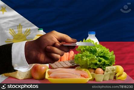 man stretching out credit card to buy food in front of complete wavy national flag of philippines