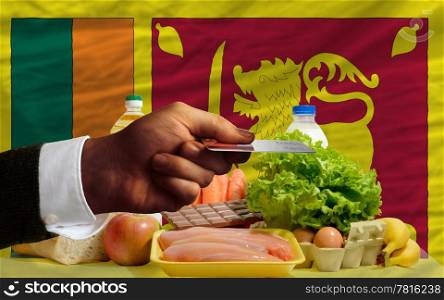 man stretching out credit card to buy food in front of complete wavy national flag of sri lanka