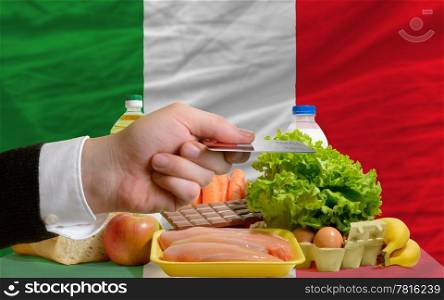 man stretching out credit card to buy food in front of complete wavy national flag of italy