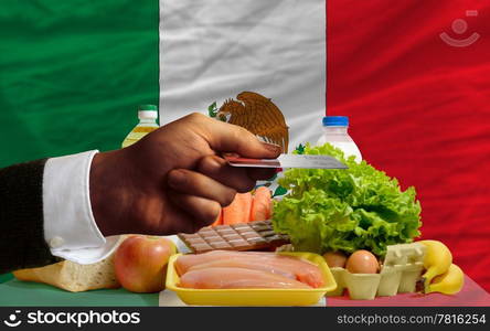 man stretching out credit card to buy food in front of complete wavy national flag of mexico