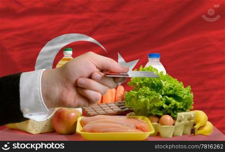 man stretching out credit card to buy food in front of complete wavy national flag of turkey