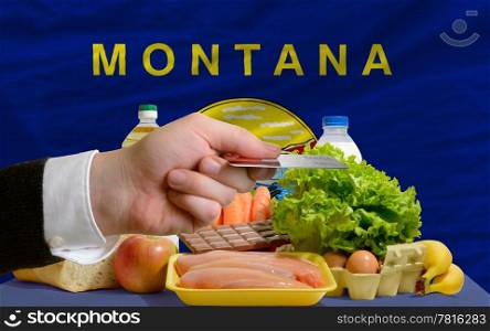 man stretching out credit card to buy food in front of complete wavy american state flag of montana