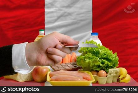man stretching out credit card to buy food in front of complete wavy national flag of peru