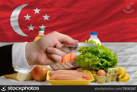man stretching out credit card to buy food in front of complete wavy national flag of singapore