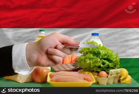 man stretching out credit card to buy food in front of complete wavy national flag of hungary