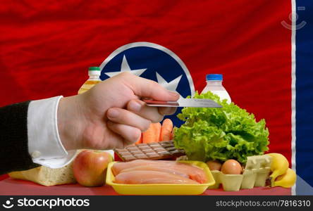 man stretching out credit card to buy food in front of complete wavy american state flag of tennessee