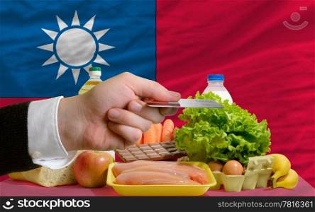 man stretching out credit card to buy food in front of complete wavy national flag of taiwan