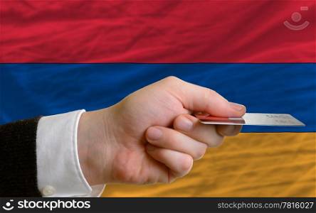 man stretching out credit card to buy goods in front of complete wavy national flag of armenia