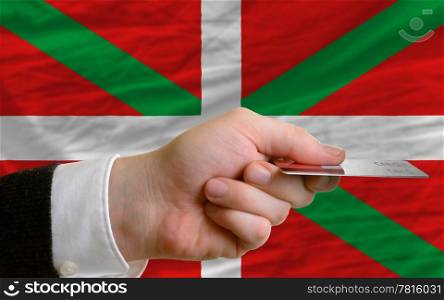 man stretching out credit card to buy goods in front of complete wavy national flag of basque