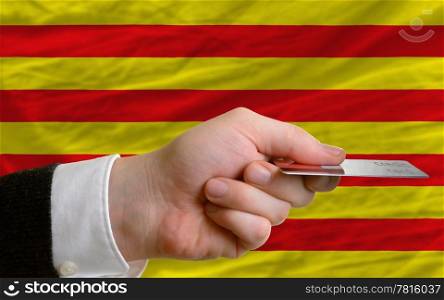 man stretching out credit card to buy goods in front of complete wavy national flag of catalonia