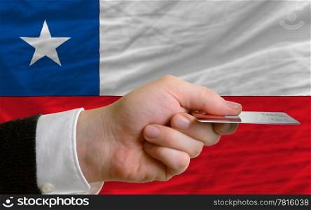man stretching out credit card to buy goods in front of complete wavy national flag of chile