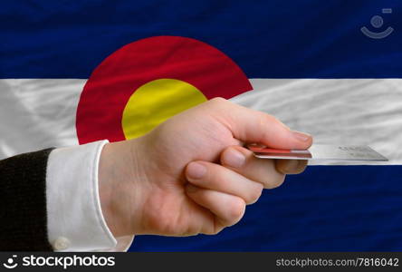 man stretching out credit card to buy goods in front of complete wavy national flag of american state of colorado