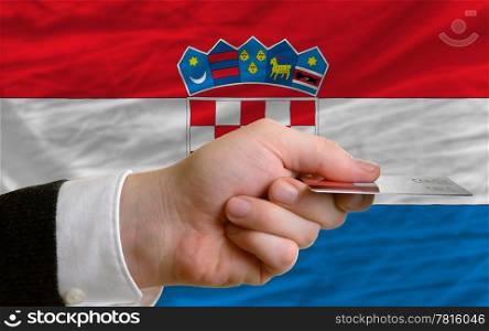 man stretching out credit card to buy goods in front of complete wavy national flag of croatia