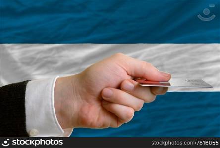 man stretching out credit card to buy goods in front of complete wavy national flag of el salvador