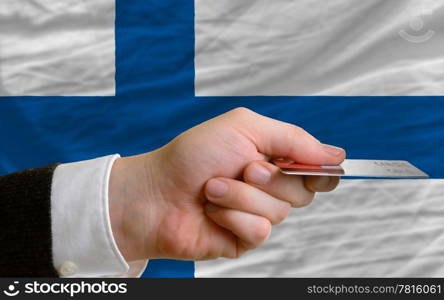 man stretching out credit card to buy goods in front of complete wavy national flag of finland