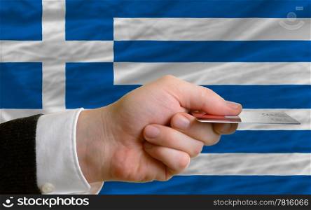 man stretching out credit card to buy goods in front of complete wavy national flag of greece