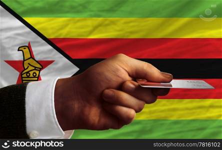 man stretching out credit card to buy goods in front of complete wavy national flag of zimbabwe