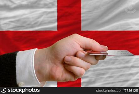 man stretching out credit card to buy goods in front of complete wavy national flag of england