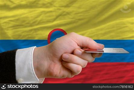man stretching out credit card to buy goods in front of complete wavy national flag of colombia