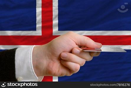 man stretching out credit card to buy goods in front of complete wavy national flag of iceland