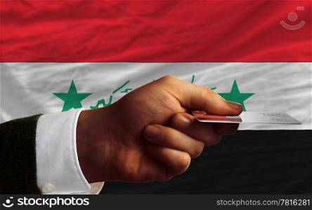 man stretching out credit card to buy goods in front of complete wavy national flag of iraq