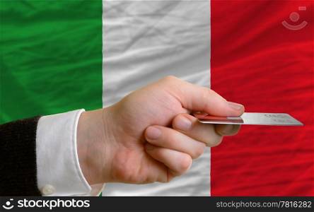 man stretching out credit card to buy goods in front of complete wavy national flag of italy