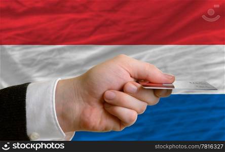 man stretching out credit card to buy goods in front of complete wavy national flag of holland