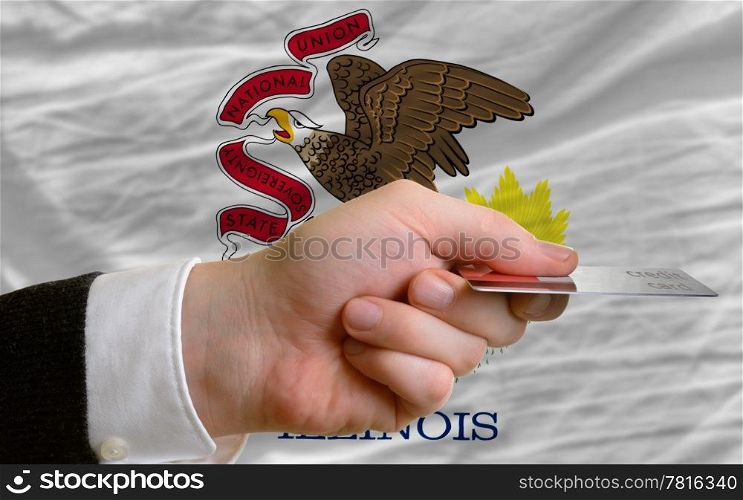 man stretching out credit card to buy goods in front of complete wavy national flag of american state of illinois