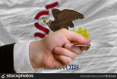 man stretching out credit card to buy goods in front of complete wavy national flag of american state of illinois