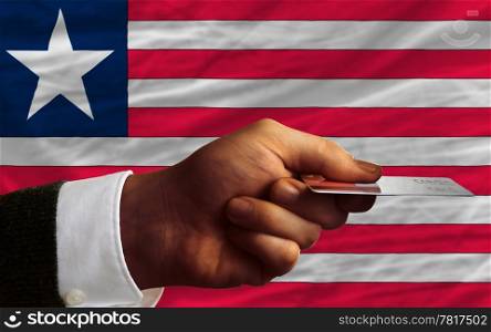 man stretching out credit card to buy goods in front of complete wavy national flag of liberia