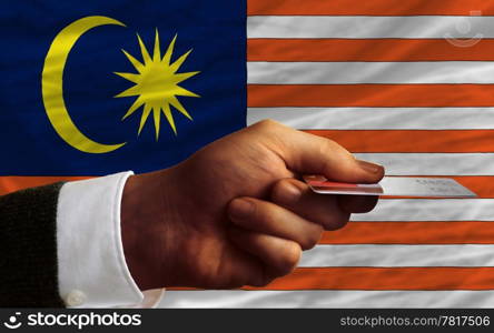 man stretching out credit card to buy goods in front of complete wavy national flag of malaysia