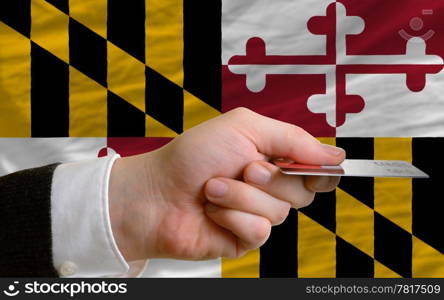 man stretching out credit card to buy goods in front of complete wavy national flag of american state of maryland