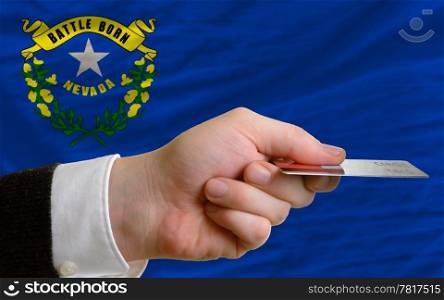 man stretching out credit card to buy goods in front of complete wavy national flag of american state of nevada