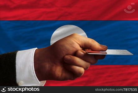 man stretching out credit card to buy goods in front of complete wavy national flag of laos