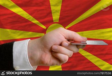 man stretching out credit card to buy goods in front of complete wavy national flag of macedonia