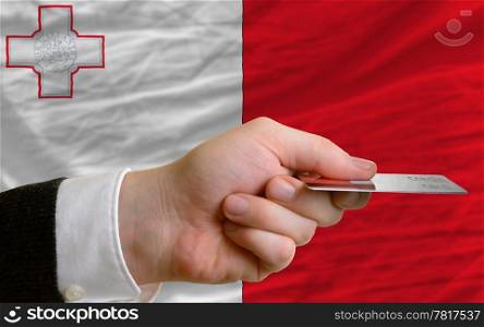 man stretching out credit card to buy goods in front of complete wavy national flag of malta