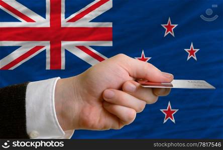 man stretching out credit card to buy goods in front of complete wavy national flag of new zealand