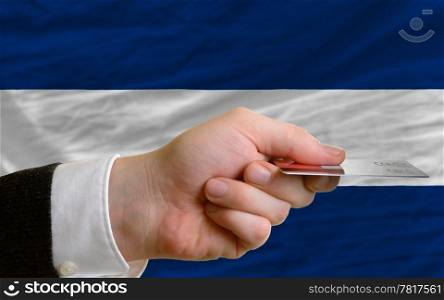 man stretching out credit card to buy goods in front of complete wavy national flag of nicaragua