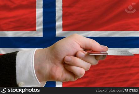 man stretching out credit card to buy goods in front of complete wavy national flag of norway