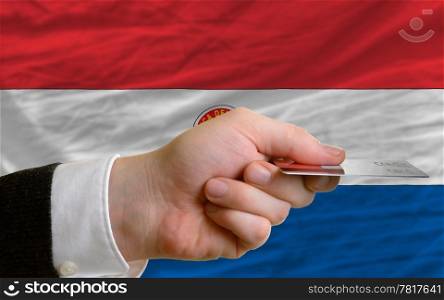 man stretching out credit card to buy goods in front of complete wavy national flag of paraguay